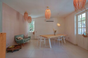 A dining area with a wooden table and white chairs, a green patterned sofa, and hanging orange lamps. - Maison Del Sole (Quartu Sant'Elena)