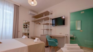 A hotel room with two beds, a desk, a chair, a TV, and a bathroom with a green wall. - Maison Del Sole (Quartu Sant'Elena)