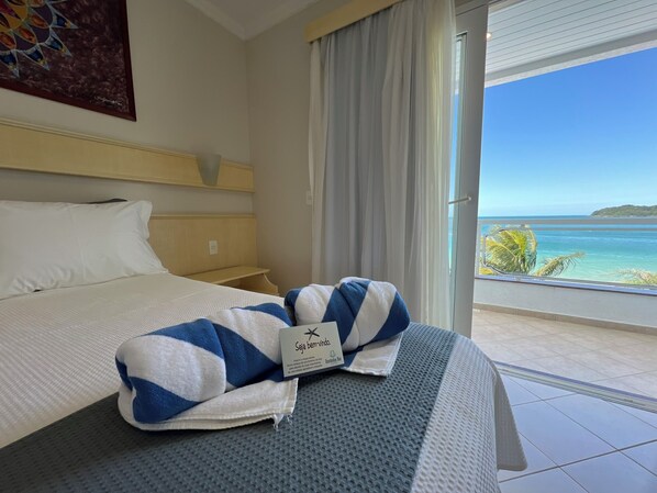 A hotel room with a bed, a window with a view of the sea, and a towel on the bed.