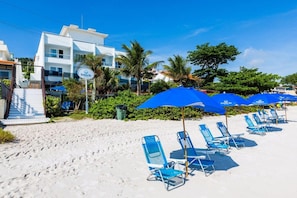 A beachside hotel with a white building, blue umbrellas, and beach chairs.