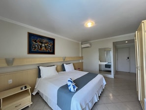 A hotel room with a bed, bedside table, wall art, and an air conditioning unit.