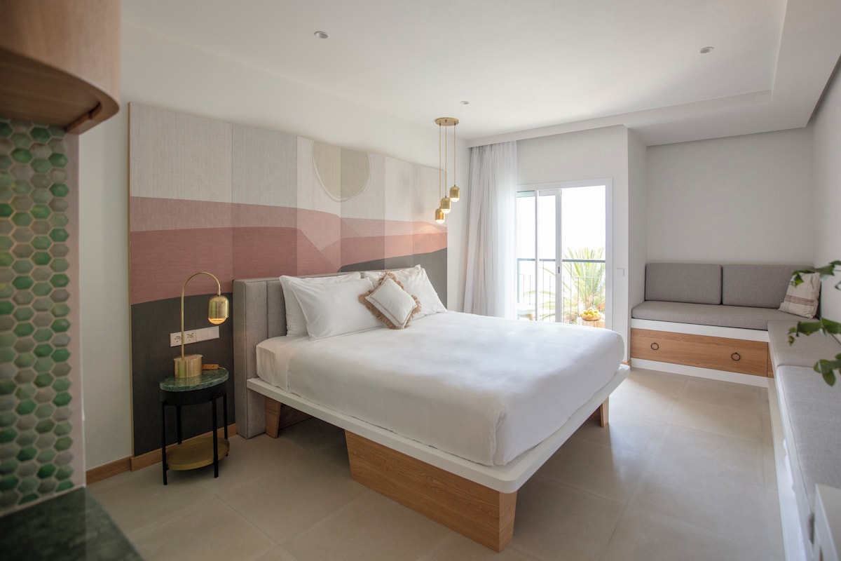 Een moderne slaapkamer met een groot bed, nachtkastjes, een ingebouwde bank en een balkon met uitzicht.