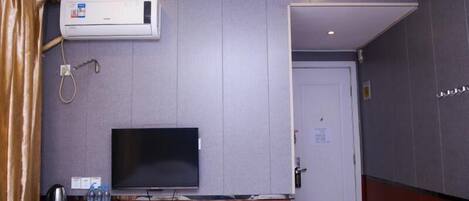 A hotel room with a flat-screen TV, a desk with a coffee maker, water bottles, and a small table.