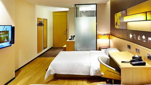 A hotel room with two beds, a desk, a chair, a TV, and a bathroom visible through a glass door. - 7 Days Premium (Shenzhen)