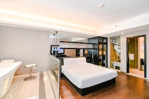 A modern hotel room with a large bed, a desk, and a glass partition separating the bedroom from the bathroom.