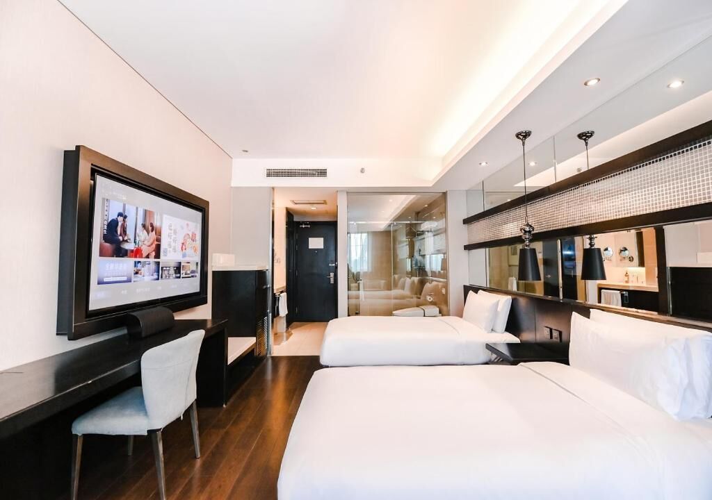Ein Hotelzimmer mit großem Flachbildfernseher, Schreibtisch, zwei Betten, einem Spiegel und modernem Design.