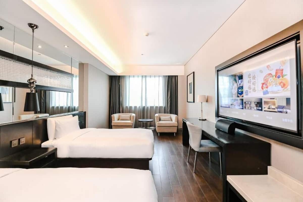 A hotel room with two beds, a desk, a chair, a TV, and a window with curtains.