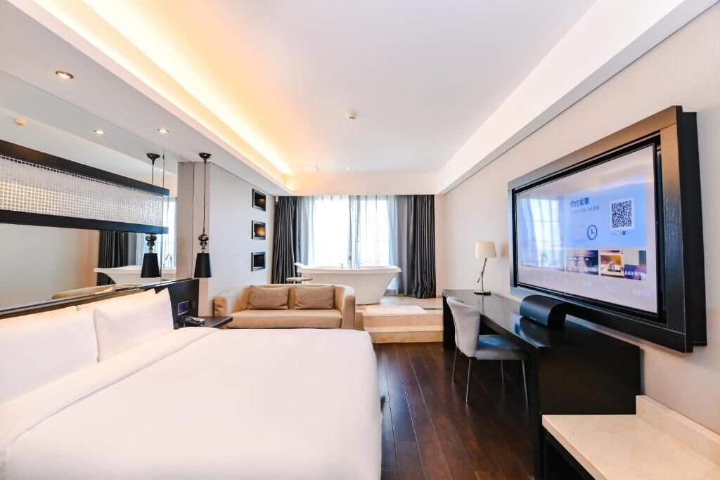 Une chambre d’hôtel moderne équipée d’un grand lit, d’un canapé, d’un bureau et d’un écran de télévision affichant un code QR.