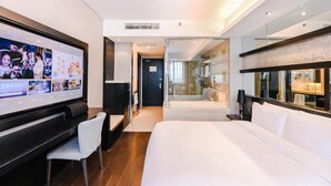 A modern hotel room with a large bed, a TV, a desk, and a glass partition leading to a bathroom. - Crystal Orange Intl. Tourist Resort (Shanghai)
