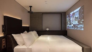 A modern hotel room with a large bed, a flat-screen TV mounted on the wall, and a ceiling-mounted projector. - Fenk Attitude Hotel (Guangzhou)