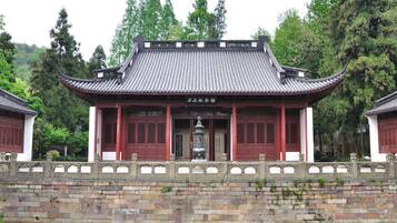 A traditional Chinese building with a tiled roof, red columns, and a stone bridge in front.