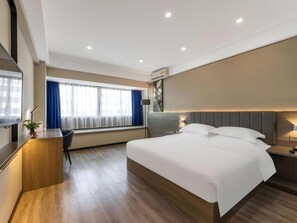 Ein modernes Hotelzimmer mit einem großen Bett, einem Schreibtisch und einem Fenster mit Vorhängen.