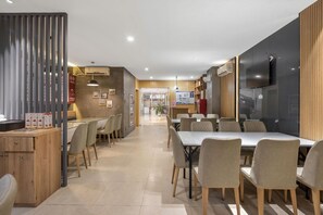 Uma área de refeições moderna com uma mesa comprida e cadeiras, uma divisória de madeira com um menu e uma TV fixada na parede.