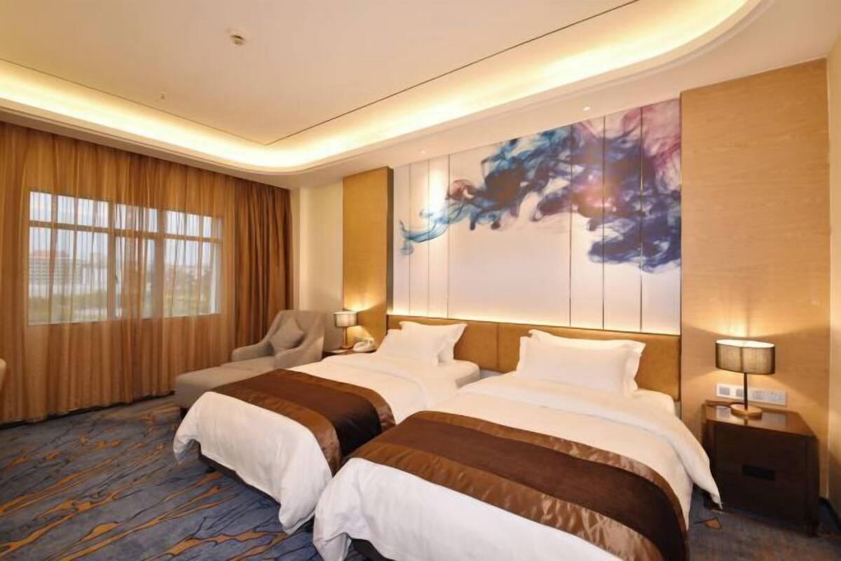 Ein Hotelzimmer mit zwei Betten, einem großen Fenster mit Vorhängen, einem Wandbild und einem Teppichboden.