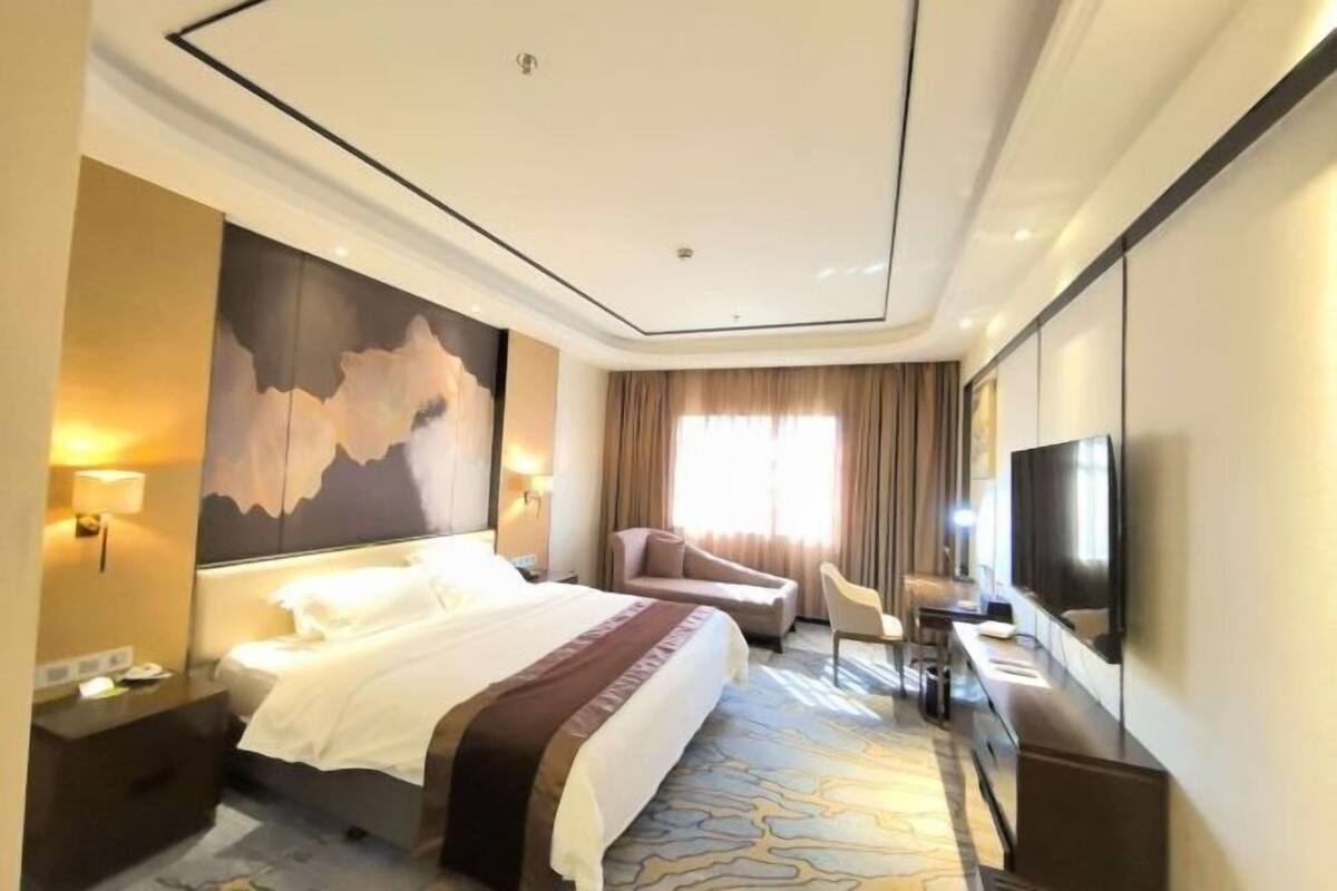 Ein Hotelzimmer mit einem großen Bett, einem Schreibtisch, einem Stuhl, einem Fernseher und einem Bild an der Wand.