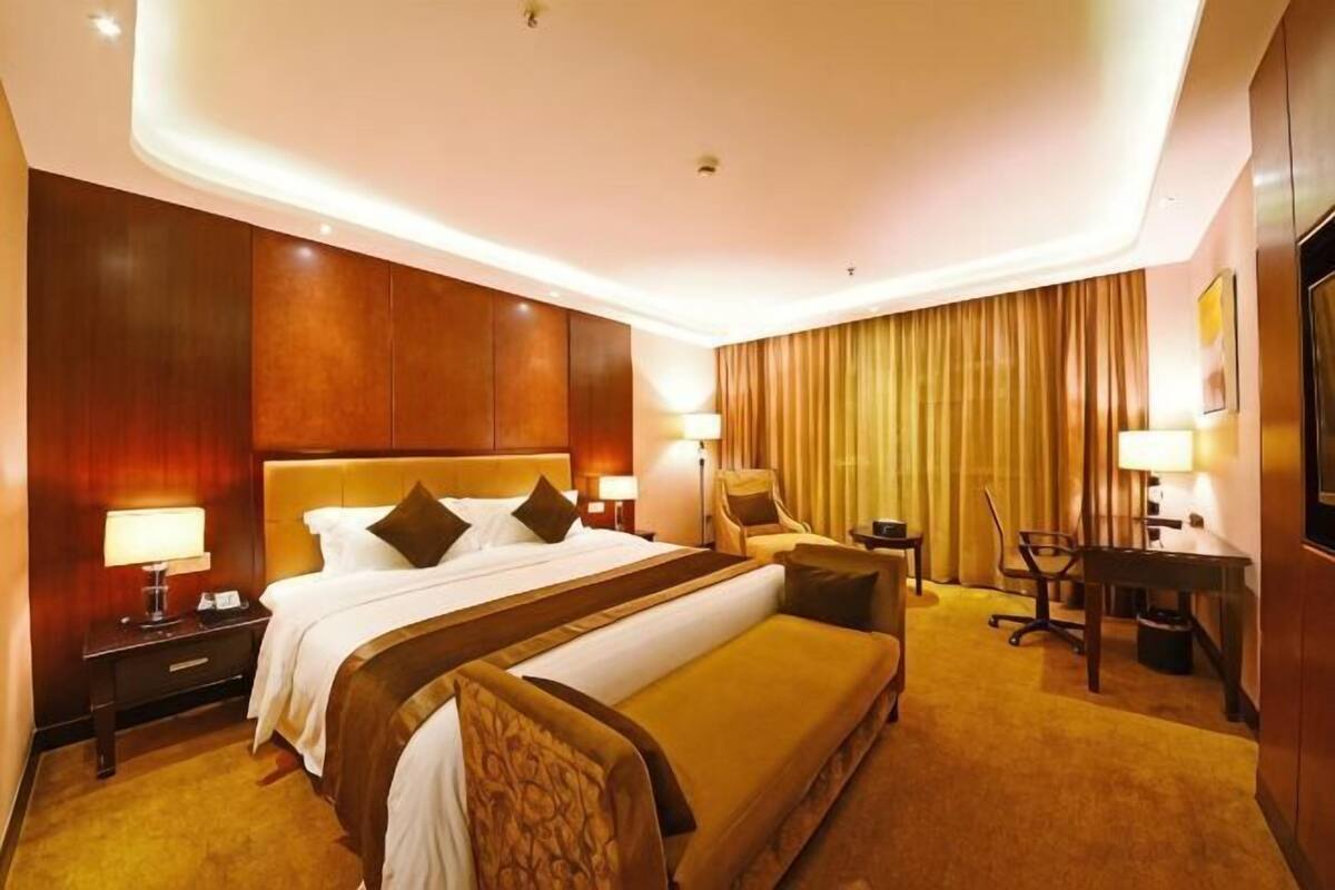 Ein Hotelzimmer mit einem großen Bett, Nachttischen, einem Schreibtisch, einem Sessel und einem Fernseher.