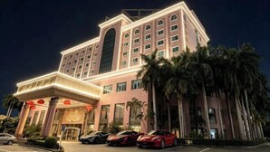 Een hotel met meerdere verdiepingen, een opvallende ingang, palmbomen en een parkeerplaats met auto's.