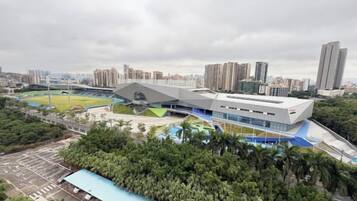 A modern building with a unique roof structure, surrounded by greenery and urban buildings.