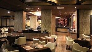 Een restaurant met een modern interieur, met een bar in het midden, verschillende zithoeken en warme sfeerverlichting.