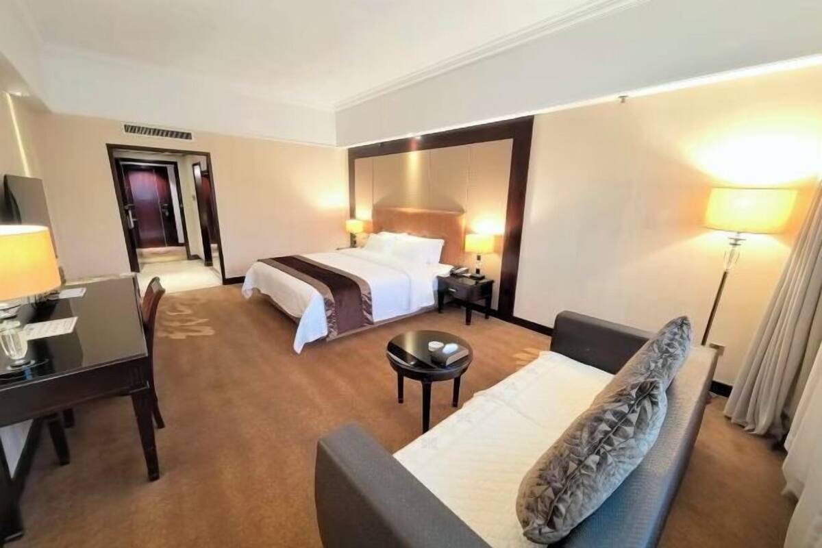 Ein Hotelzimmer mit Bett, Nachttischen, Schreibtisch, Stuhl, Sofa und Lampe.