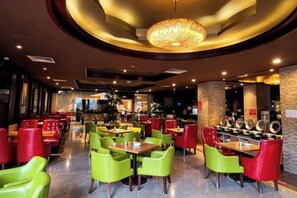 A restaurant interior with round tables, red and green chairs, and a central chandelier.