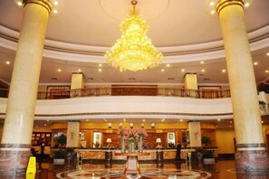 A hotel lobby with a grand chandelier, marble columns, and a reception desk.