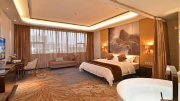 A hotel room with a large bed, a sitting area with a sofa, a desk with a chair, a large window with curtains, and a bathtub.