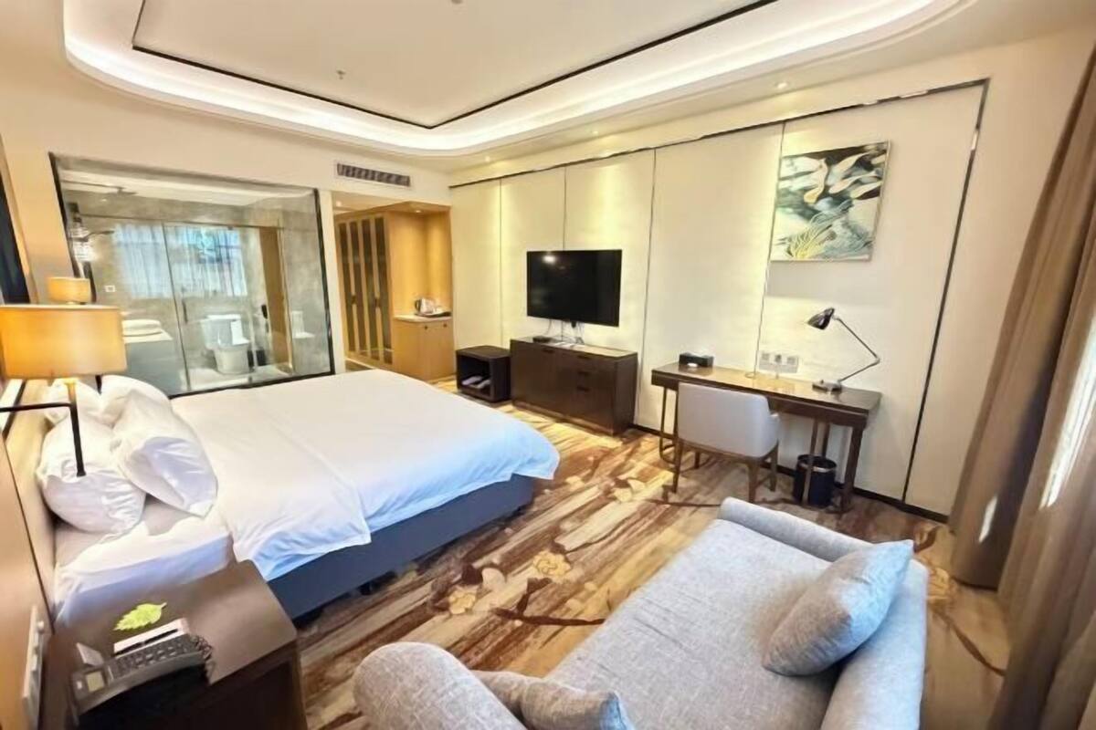 Ein Hotelzimmer mit Bett, Schreibtisch, Fernseher, Sofa und Spiegel.