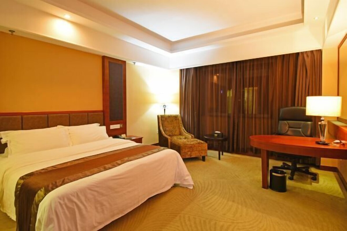 Une chambre d’hôtel avec un grand lit, un bureau, une chaise et une petite table avec une lampe.