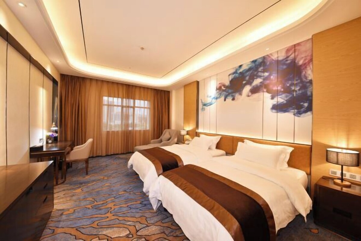 Une chambre d’hôtel avec deux lits, un bureau, une chaise et un grand tableau abstrait accroché au mur.