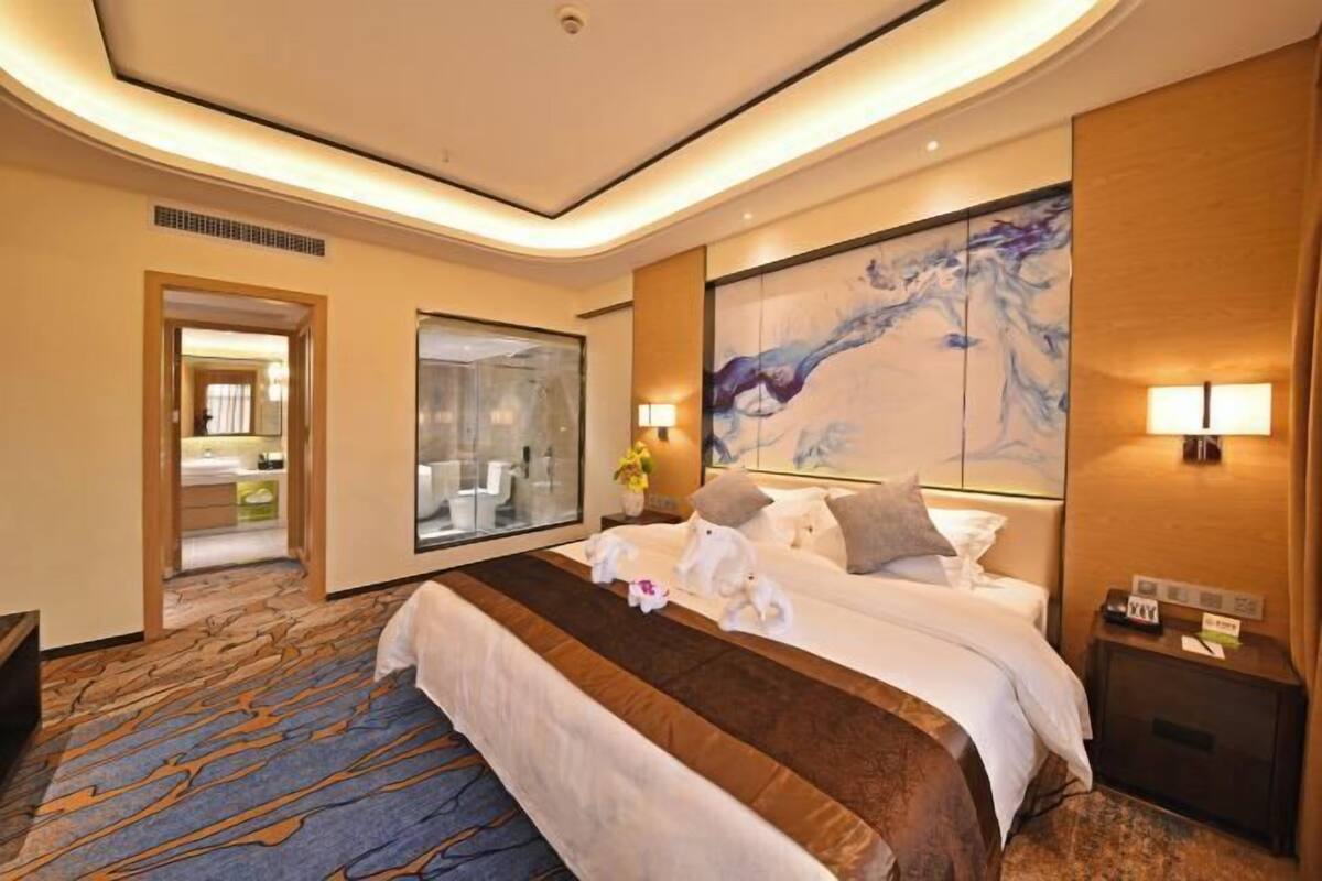 Ein Hotelzimmer mit einem großen Bett, einer Glasdusche und einem großen, abstrakten Gemälde an der Wand.
