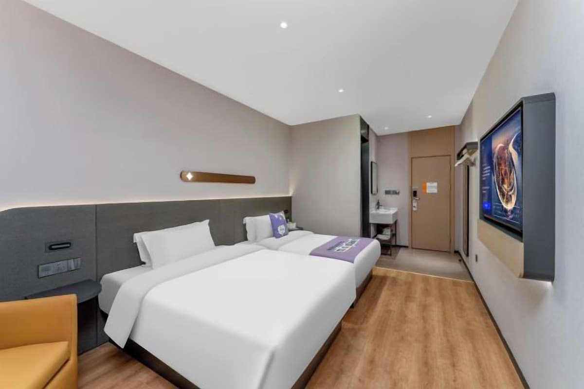 A modern hotel room with a large bed, a bedside table, a chair, a desk, and a bathroom visible through an open door.