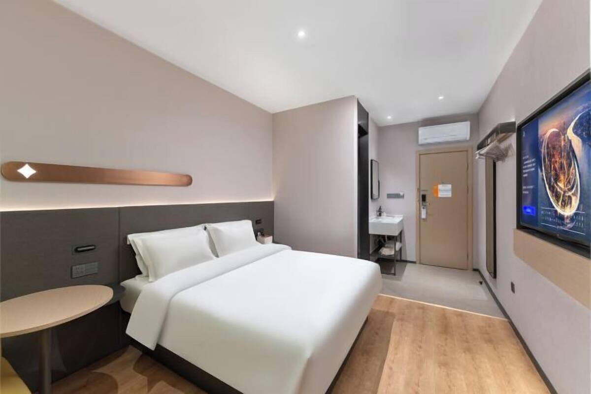 A modern hotel room with a bed, bedside table, and a large screen displaying a movie.