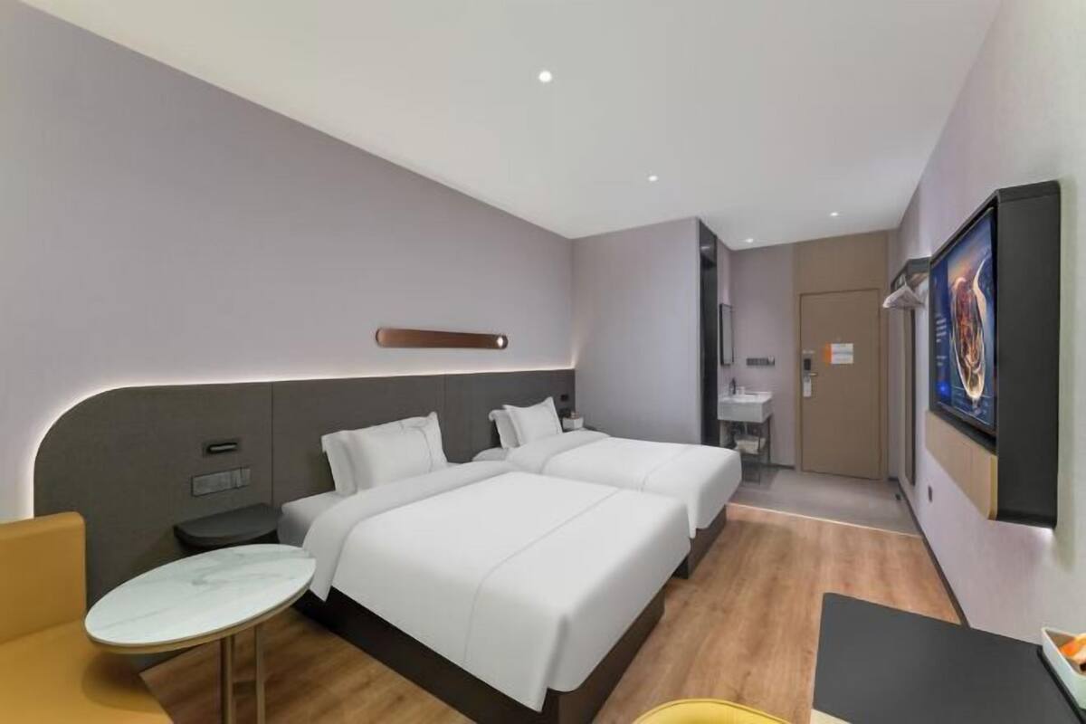 A hotel room with two beds, a small table, a sofa, a TV, and a bathroom.