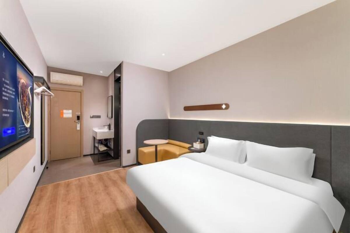 A modern hotel room with a large bed, a small seating area, a TV, and a bathroom.
