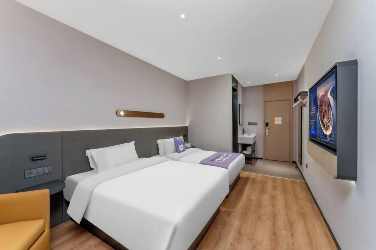 A modern hotel room with a large bed, a bedside table, a chair, a desk, and a bathroom visible through an open door.