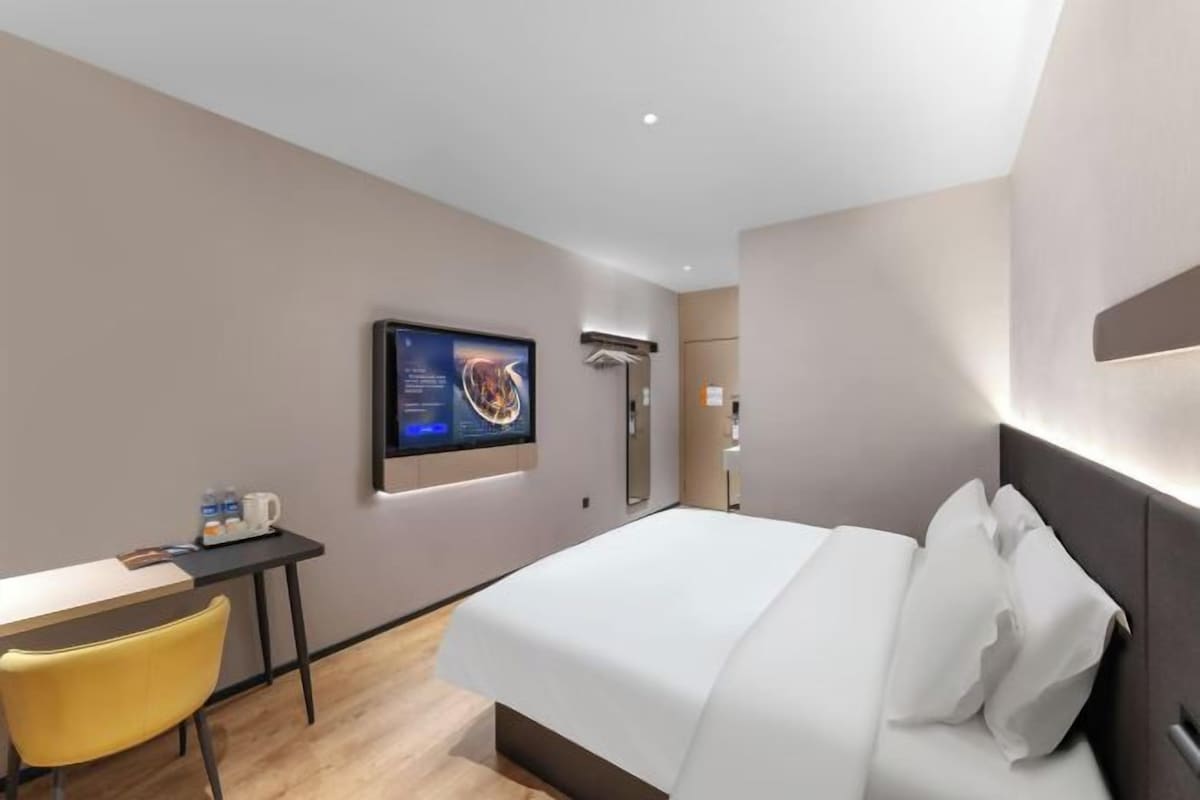 A modern hotel room with a bed, a desk, a chair, a flat-screen TV, and a shower area.