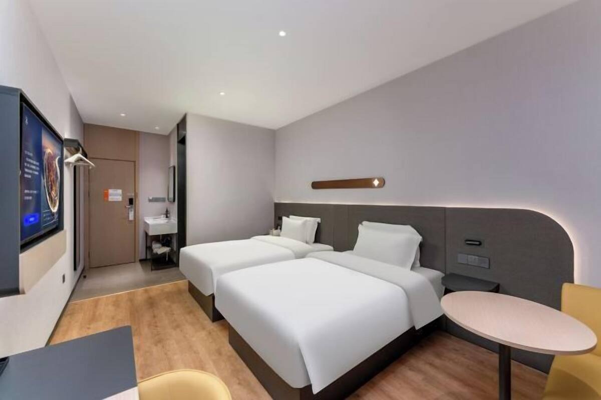 A modern hotel room with two beds, a small table, and a TV.