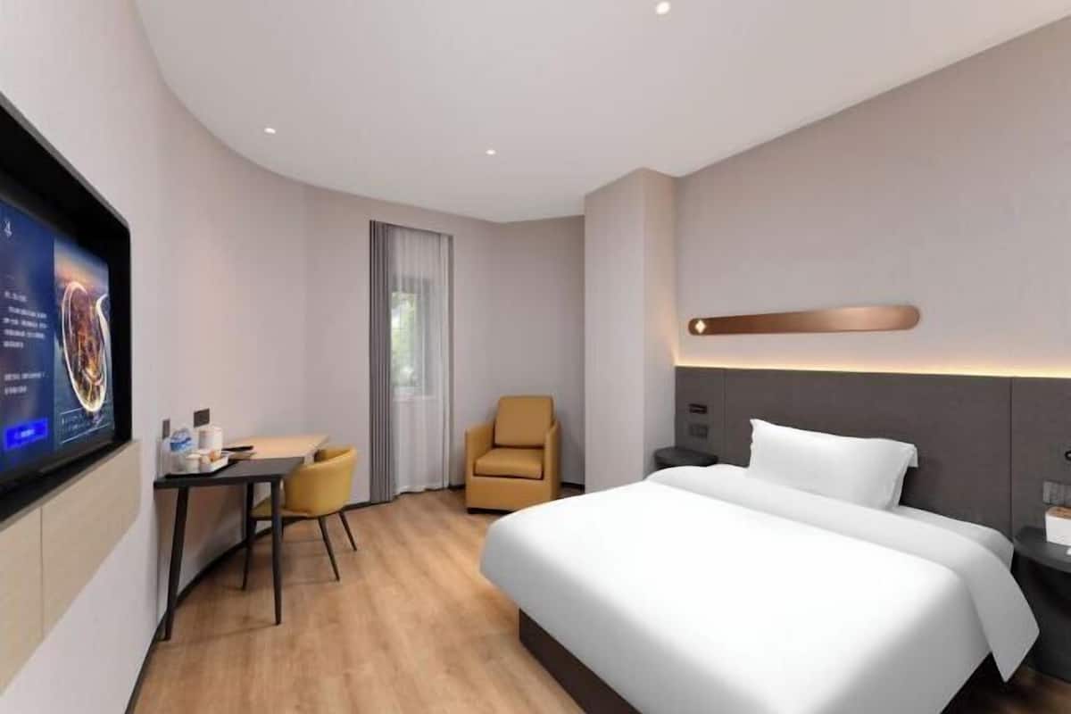 A hotel room with a bed, a desk, a chair, and a TV.