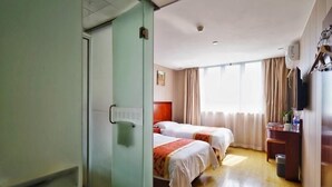 A hotel room with two beds, a wooden floor, a desk with a chair, a television, and a window with curtains.