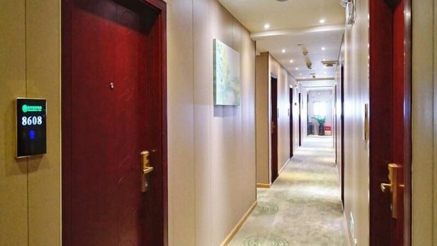A hotel corridor with a red door, a digital sign displaying room number 8608, and a carpet with circular patterns.