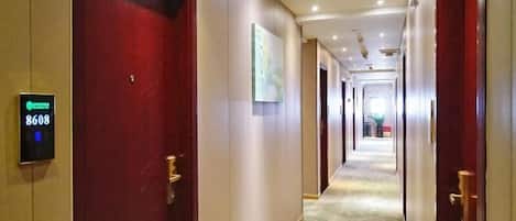 A hotel corridor with a red door, a digital sign displaying room number 8608, and a carpet with circular patterns.