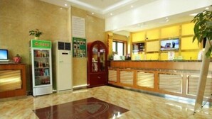 A hotel lobby with a reception desk, a vending machine, a refrigerator, and a plant.