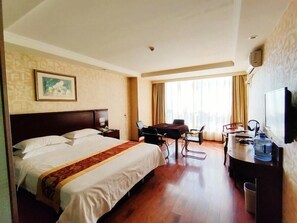 Une chambre d’hôtel avec un grand lit, un bureau avec une chaise, une télévision et une fenêtre avec des rideaux.