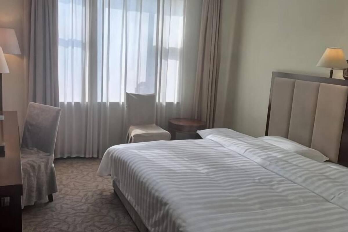 Una habitación de hotel con una cama grande, una silla, una mesita y una ventana con cortinas.