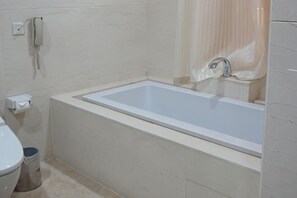 A bathroom with a bathtub, toilet, and a phone on the wall. - Furunge Hotel (Qingdao)