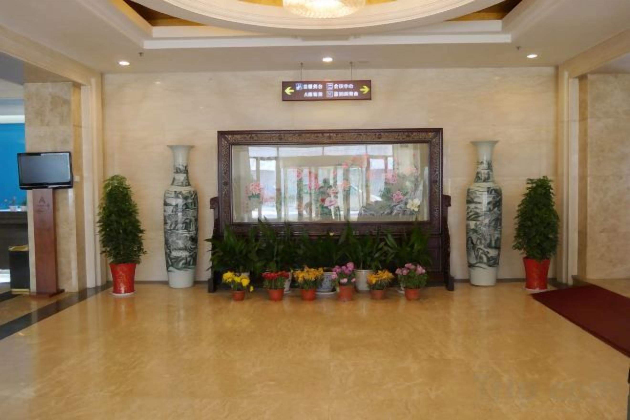 A lobby with a reception desk, potted plants, and a large mirror.