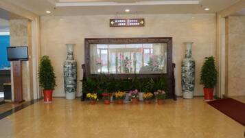 A lobby with a reception desk, potted plants, and a large mirror.