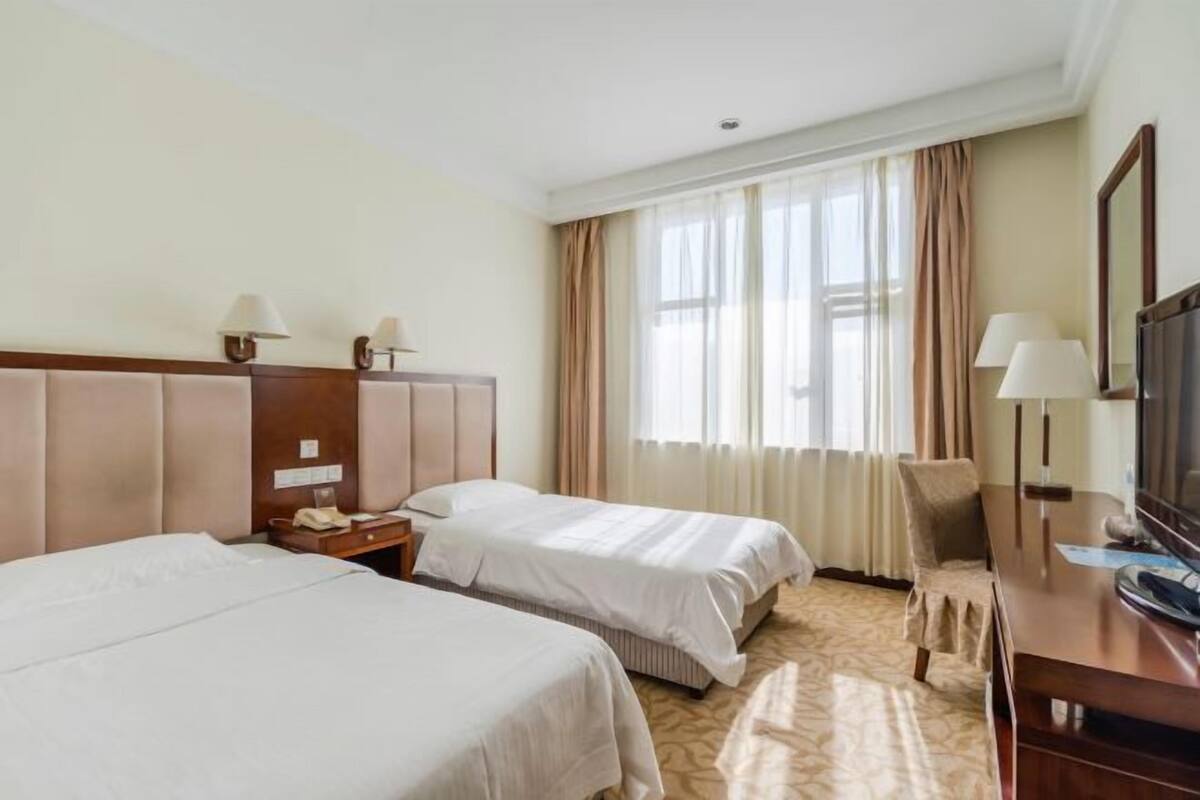 Habitación de hotel con dos camas, un escritorio, una silla, un televisor y una ventana con cortinas.