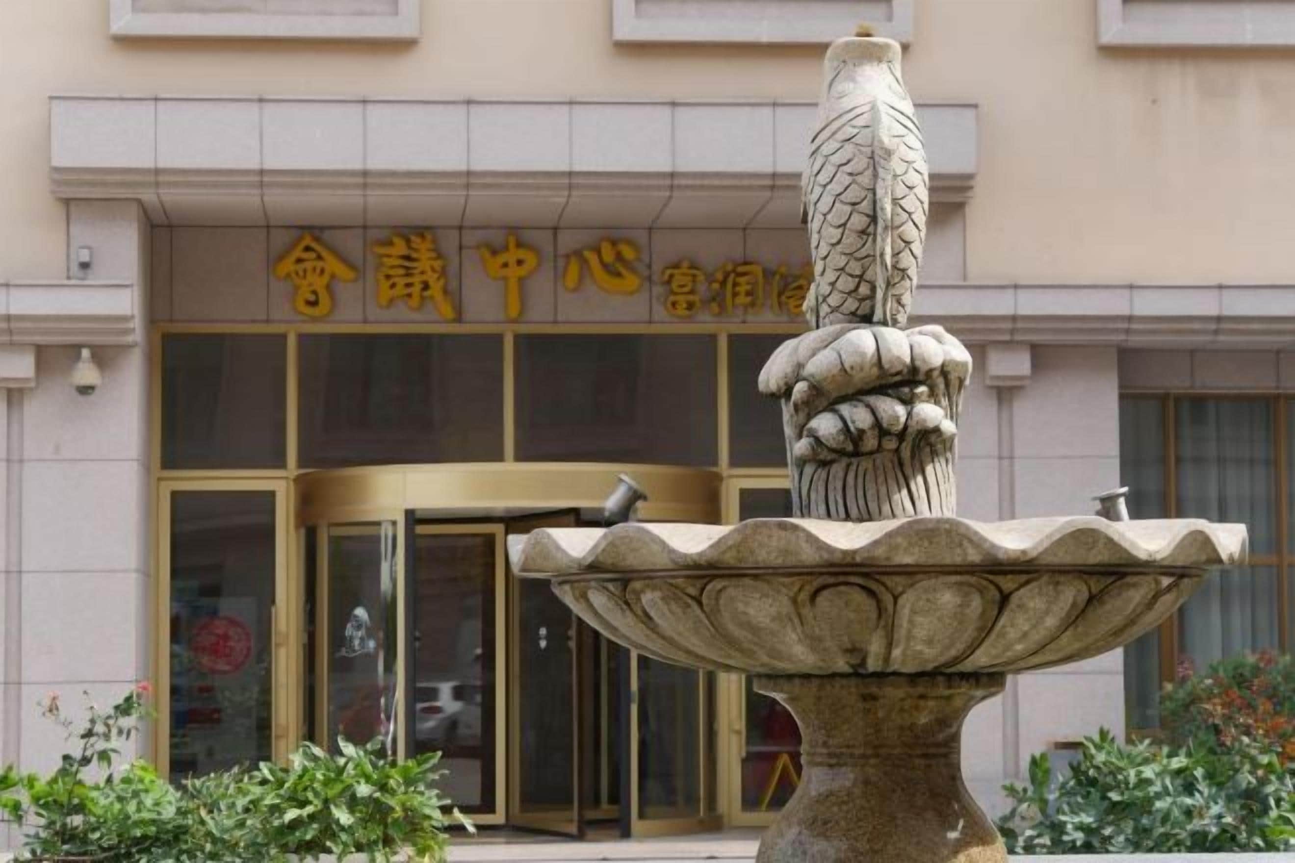 A stone fountain with a decorative top, in front of a building with a sign in a foreign language.